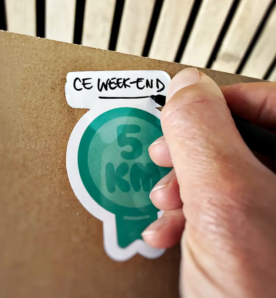 Une main écrit sur un sticker apposé sur la boîte Run, Art & Box.